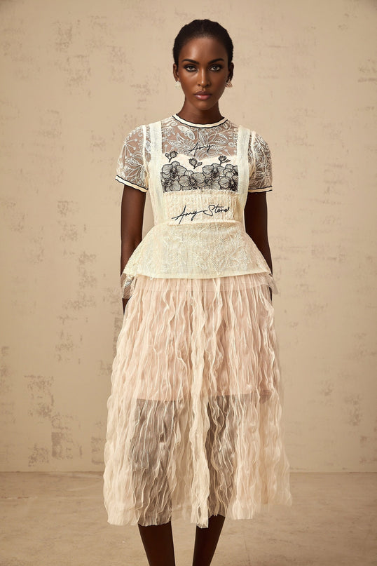 Woman wearing beige midi dress with embroidered tulle overlay standing in relaxed pose