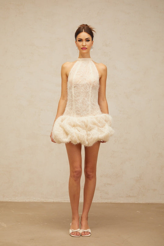 Woman wearing beige textured mini dress with puff sleeves and gathered fabric detail standing against neutral background