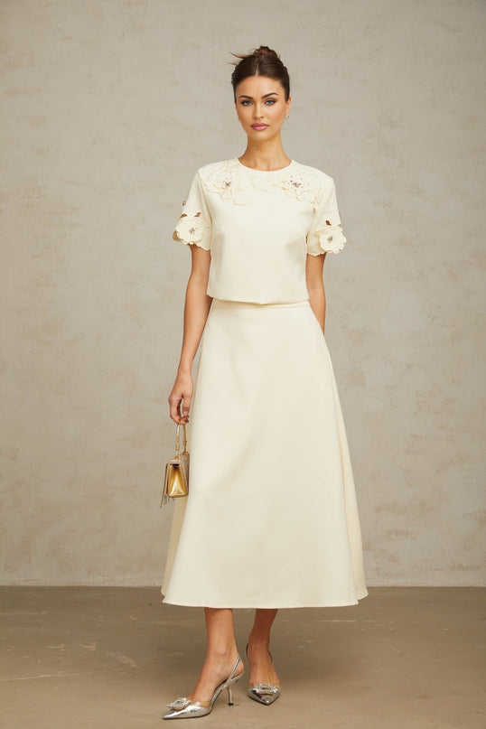 Woman wearing beige twopiece outfit with textured floral design top and matching skirt