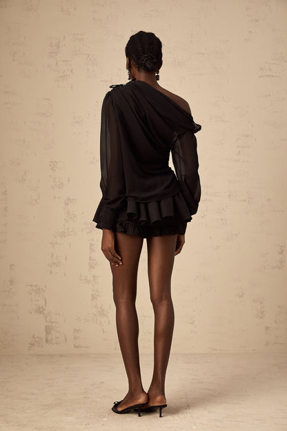 Woman wearing black asymmetric tulle blouse and matching skirt set named Andrea
