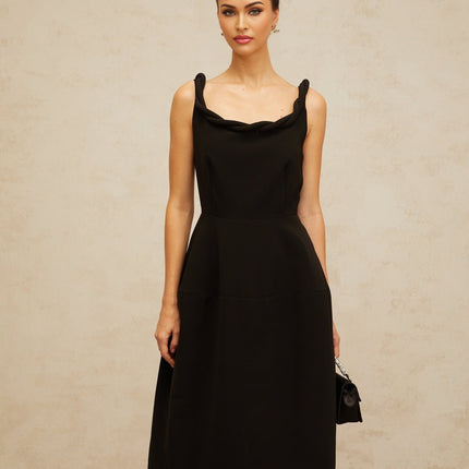 Woman wearing black braided puff sleeve midi dress with fitted bodice and flared skirt standing against plain background