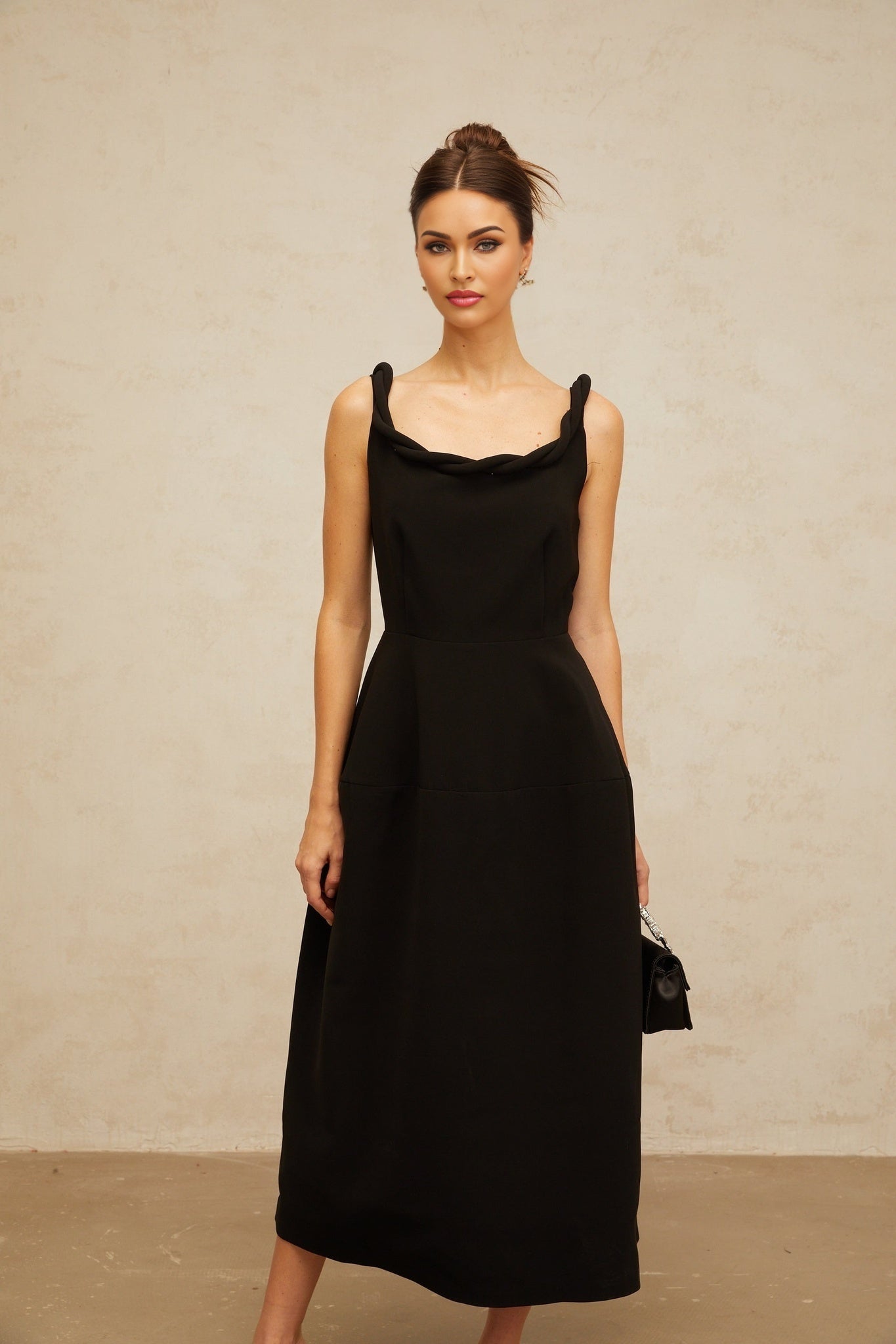 Woman wearing black braided puff sleeve midi dress with fitted bodice and flared skirt standing against plain background