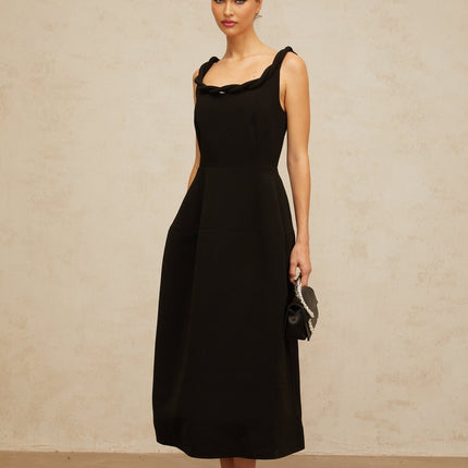 Woman wearing black braided puff sleeve midi dress with round neckline and fitted waist standing against plain background
