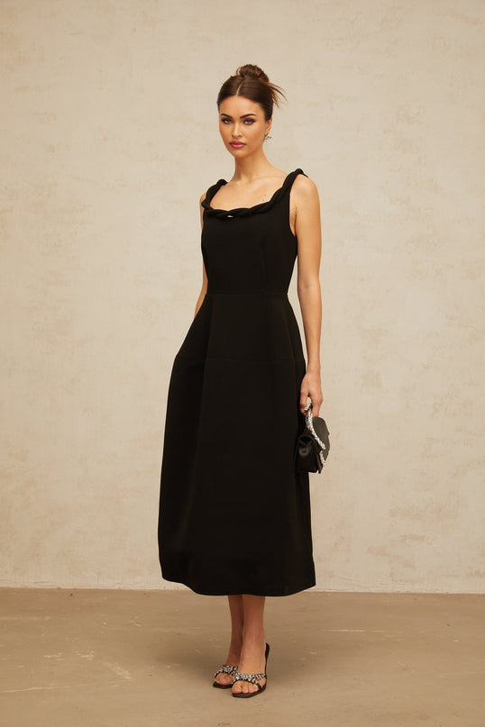 Woman wearing black braided puff sleeve midi dress with round neckline and fitted waist standing against plain background