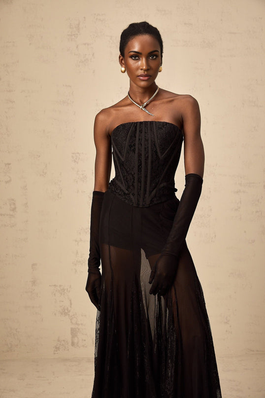 Woman wearing black floral lace corset matching skirt and gloves set against plain background