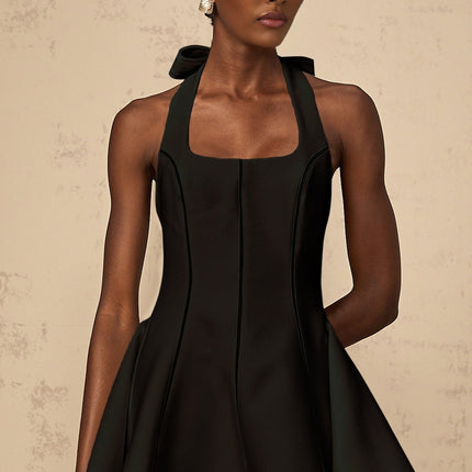 Woman wearing black halterneck mini dress with bow detail at neck