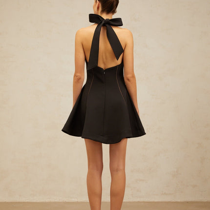 Woman wearing black halterneck mini dress with bow detail at neckline