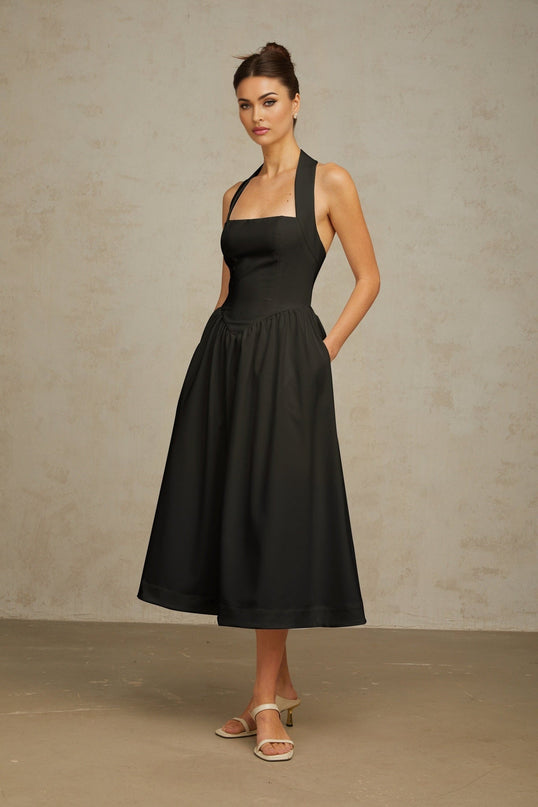 Woman wearing black halterneck pleated midi dress with fitted bodice and flowy skirt