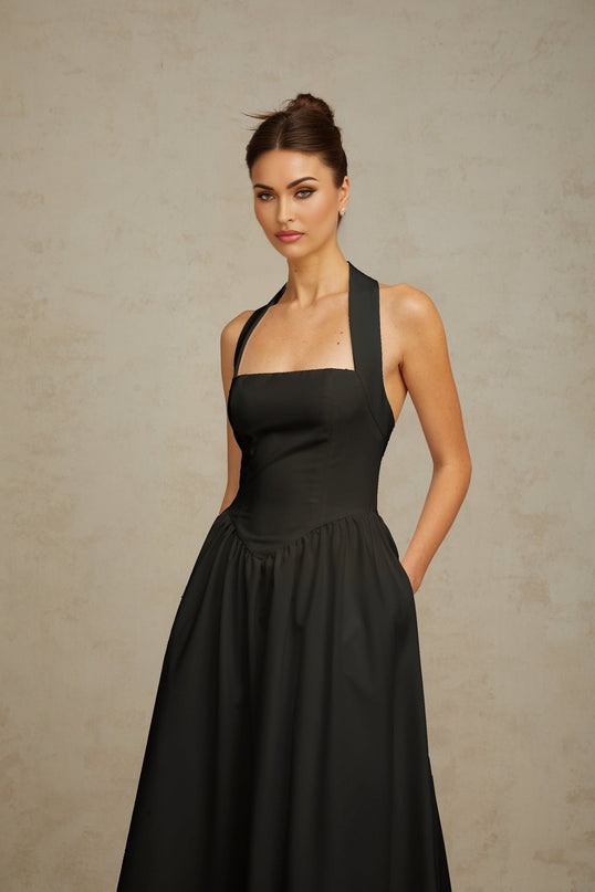 Woman wearing black halterneck pleated midi dress with fitted bodice and flowy skirt