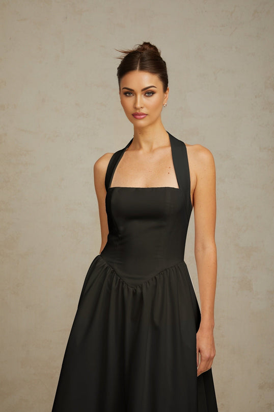 Woman wearing black halterneck pleated midi dress with fitted bodice and flowy skirt