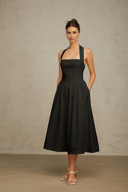 Woman wearing black halterneck pleated midi dress with fitted waist and flared skirt