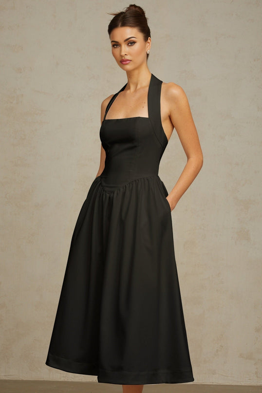 Woman wearing black halterneck pleated midi dress with fitted waist and flowing skirt