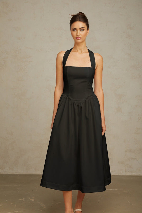 Woman wearing black halterneck pleated midi dress with fitted waist and flowy skirt