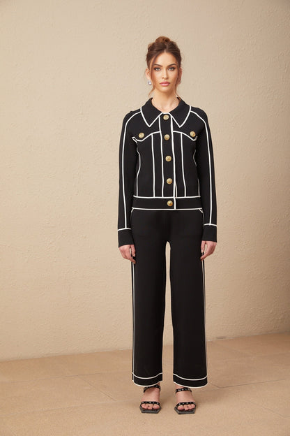 Woman wearing black jacket and trousers set with white piping detail