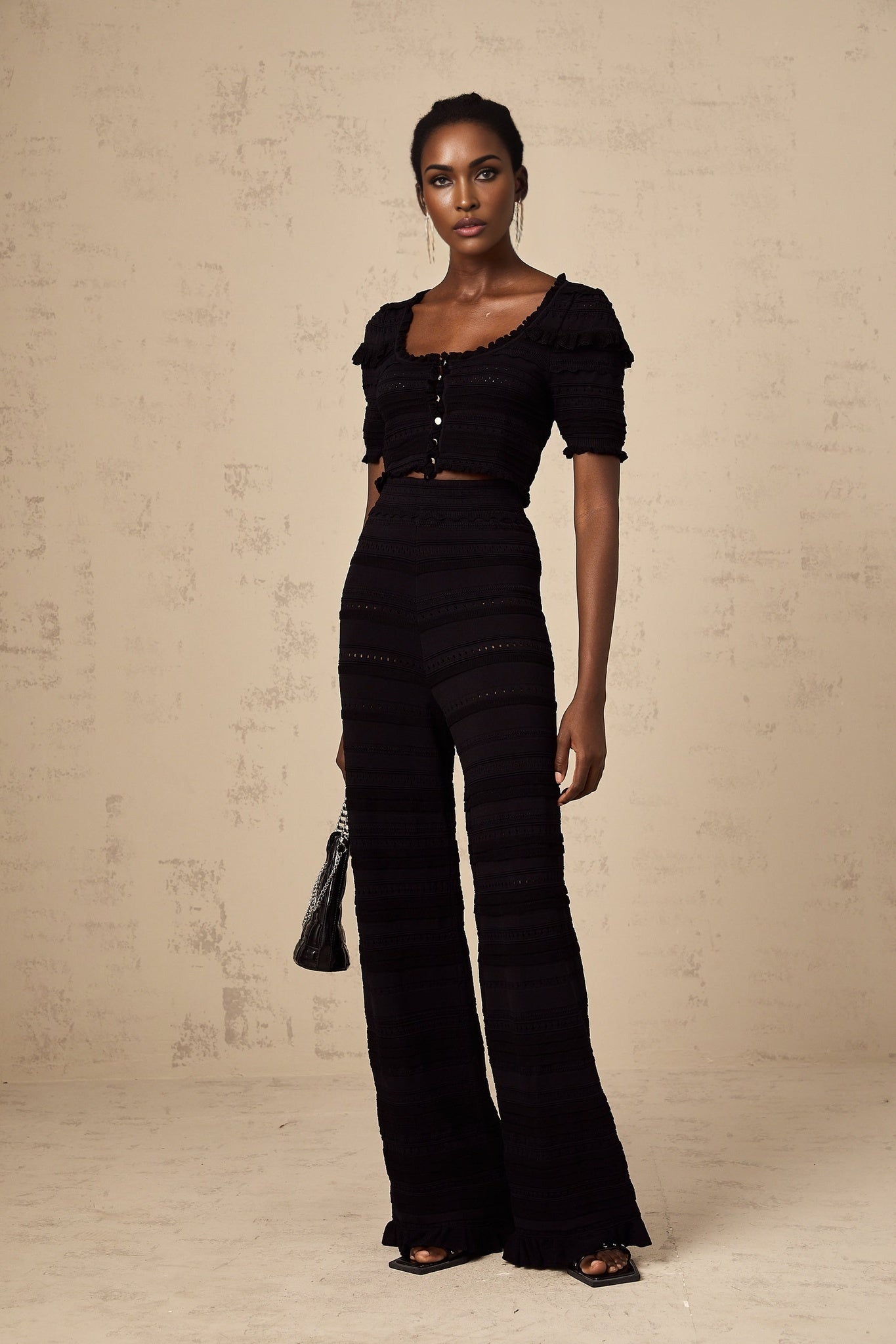 Woman wearing black knitted matching set with ruffled top and trousers