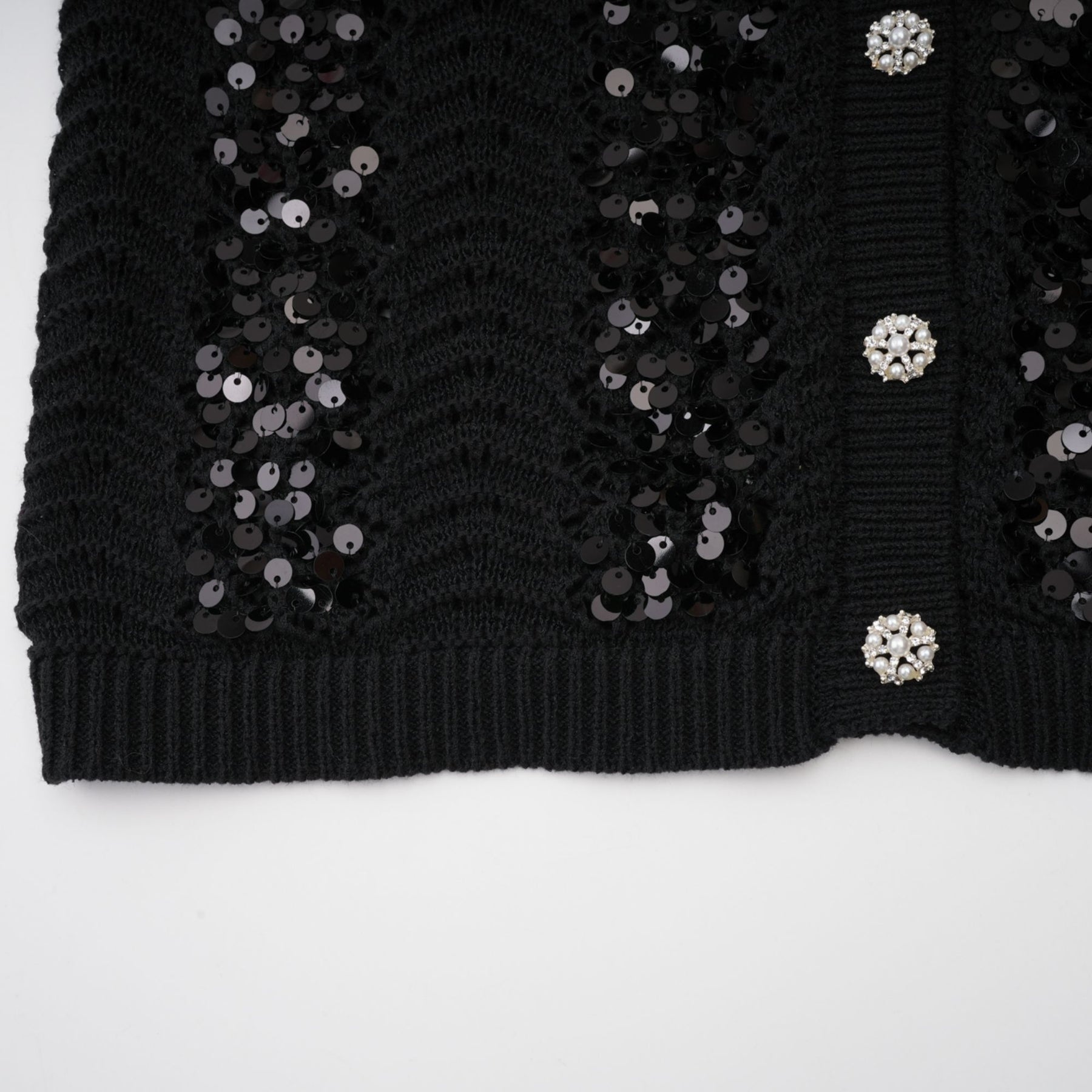 Woman wearing black sequined crochet knit cardigan and matching skirt set against plain background