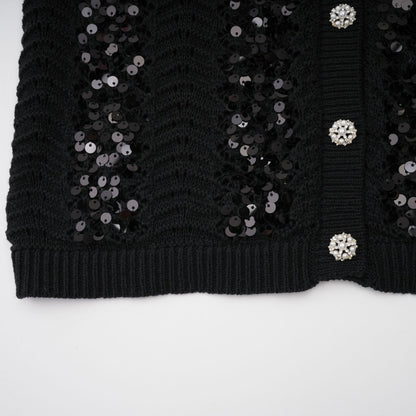 Woman wearing black sequined crochet knit cardigan and matching skirt set against plain background