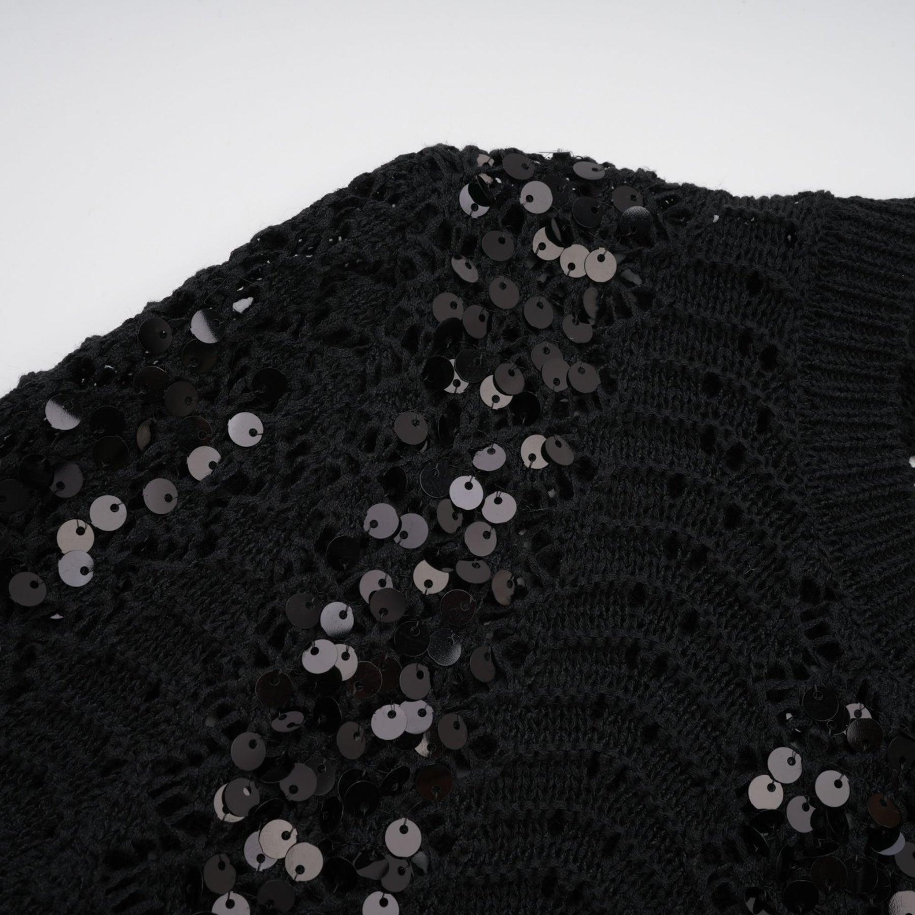 Woman wearing black sequined matching set with crochet knit cardigan and skirt