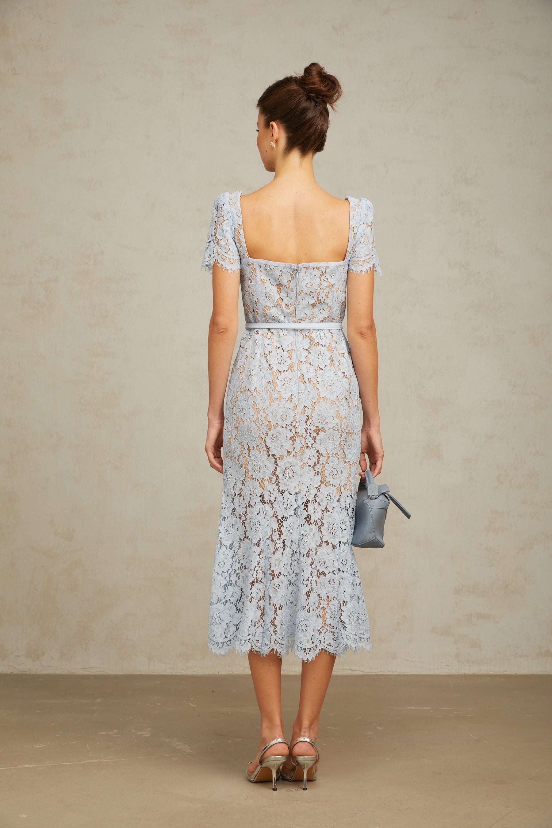 Woman wearing blue floral lace midi dress with boned bodice and fitted silhouette standing against plain background