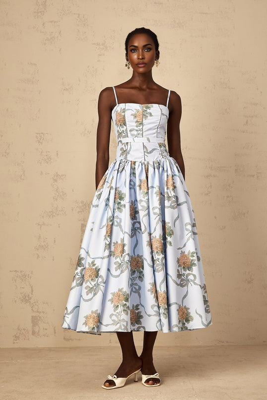 Woman wearing blue midi dress with floral print pattern standing against plain background