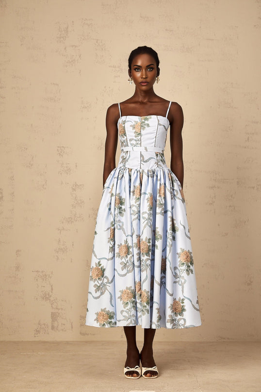 Woman wearing blue midi dress with floral print pattern standing against plain background