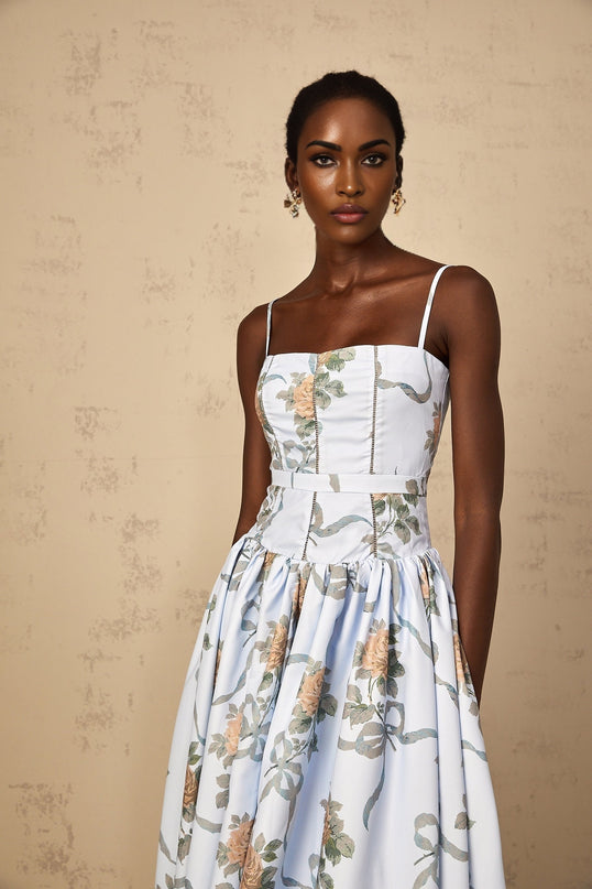 Woman wearing blue midi dress with floral print pattern standing against plain background