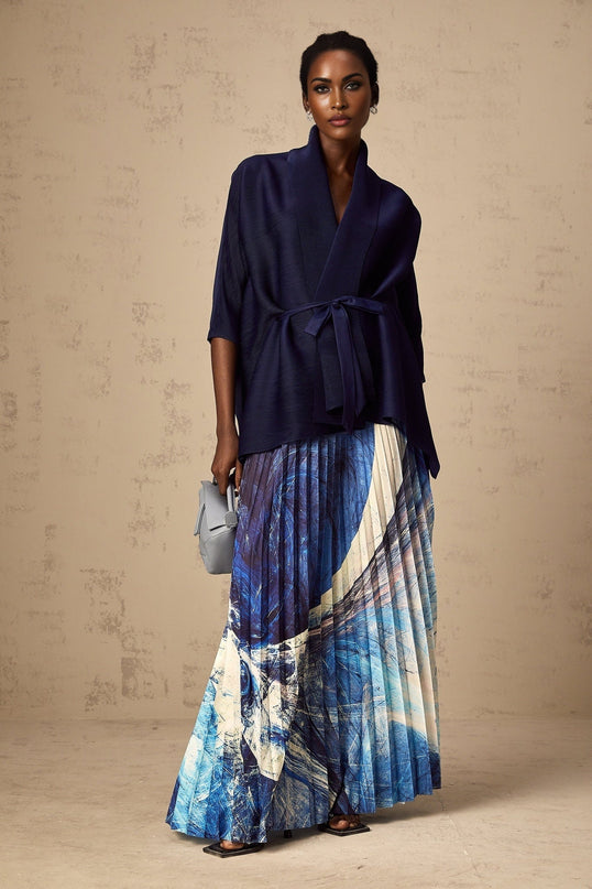 Woman wearing blue patterned cape and matching skirt set with crease detailing and allover print design