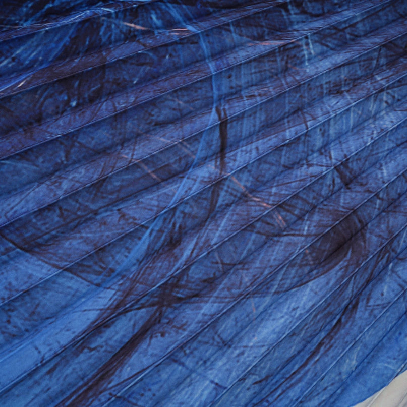 Woman wearing blue patterned cape and matching skirt set with crease details against plain background