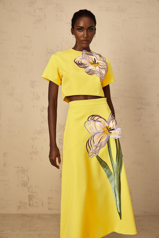 Woman wearing bright yellow twopiece outfit with floral sequin embroidery top and matching bottoms