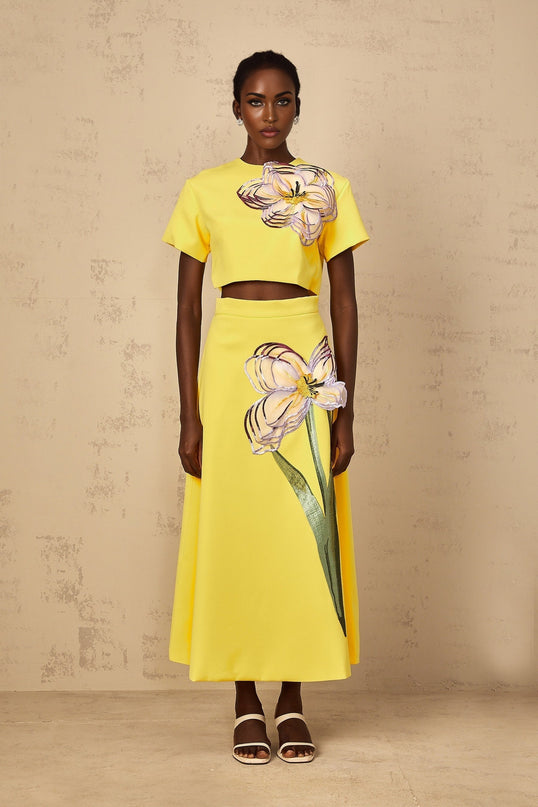 Woman wearing bright yellow twopiece outfit with sequin floral embroidery top and matching bottoms