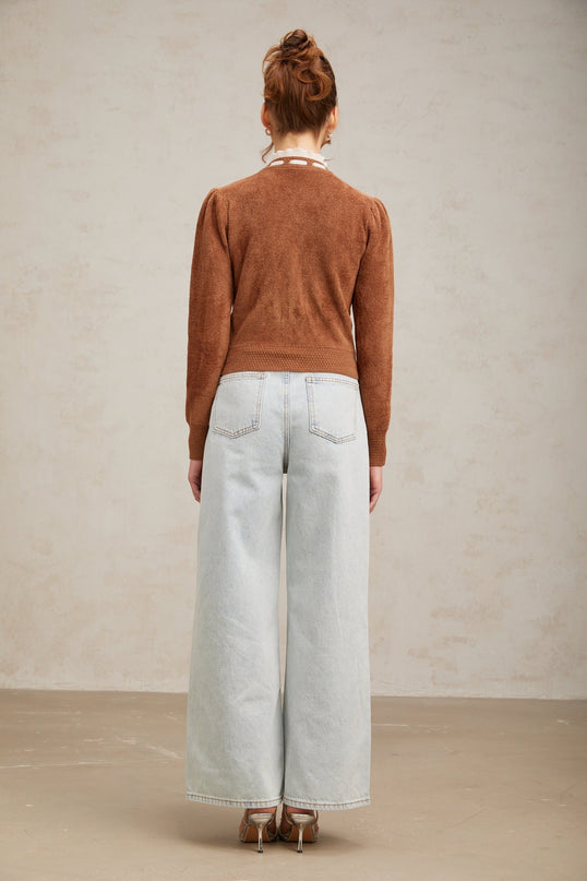 Woman wearing brown knit cardigan with embellished details and ruffled trim