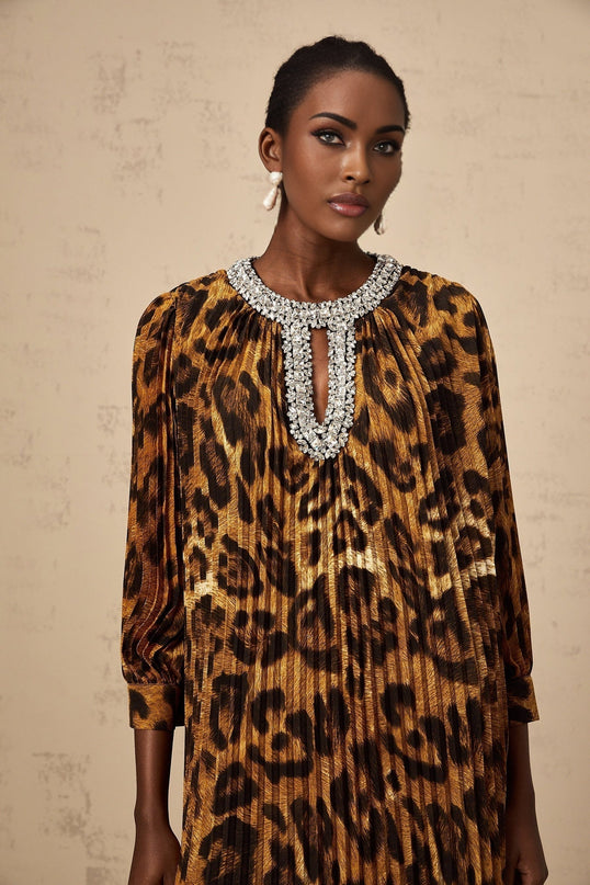 Woman wearing brown leopard print midi dress with embellishments and long sleeves standing against plain background