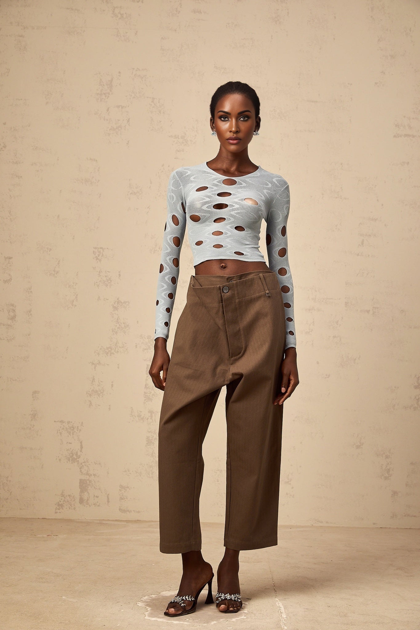 Woman wearing brown wide leg cropped trousers with shirred waistband standing against plain background