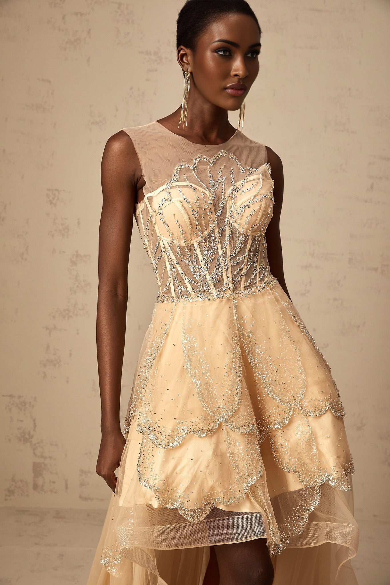 Woman wearing champagne colored sleeveless gown with embellished bodice and high low skirt with floral daisy pattern
