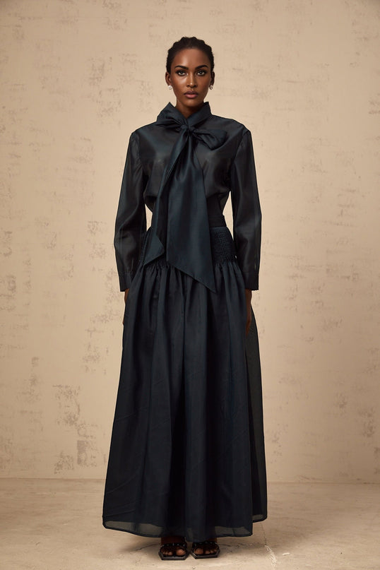 Woman wearing dark green matching set with long sleeve shirt and midi skirt ribbon tie at neck