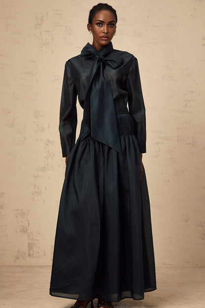 Woman wearing dark green matching shirt and skirt set with ribbon tie at neck