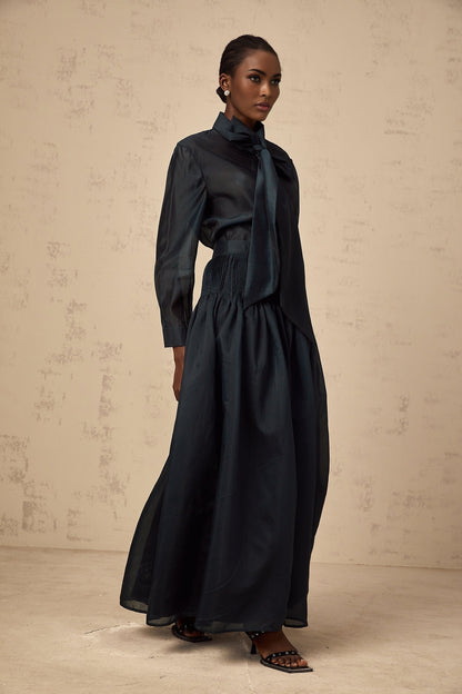 Woman wearing dark green matching shirt and skirt set with ribbon tie neck detail