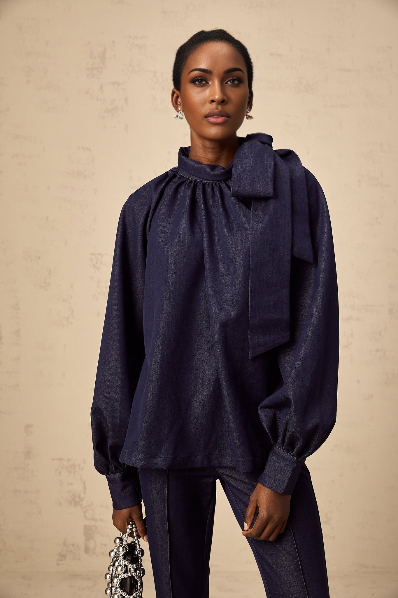 Woman wearing denim blue flared blouse and matching trousers standing against plain background