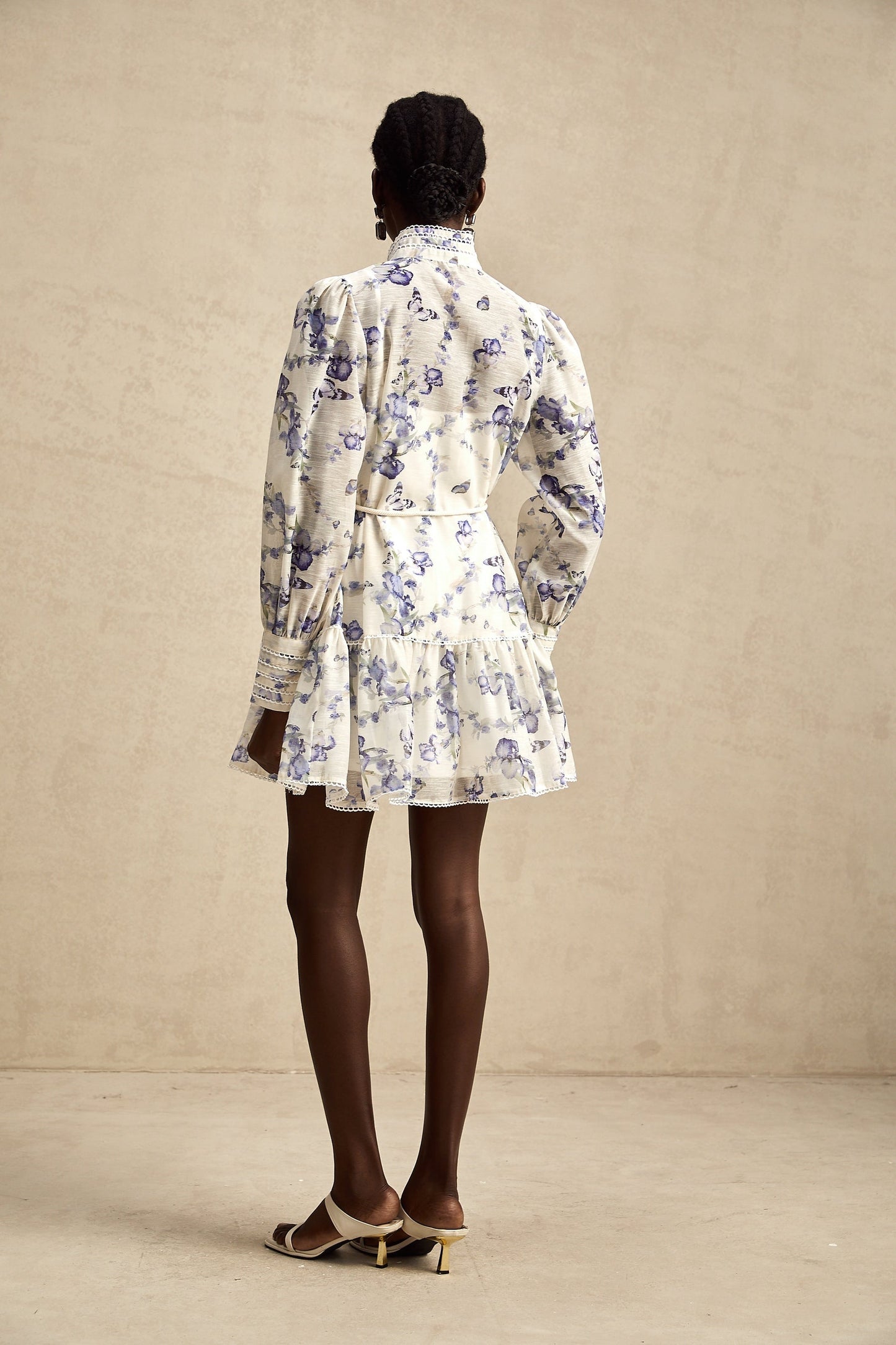 Woman wearing floral print chiffon mini dress with flared skirt and short sleeves standing against plain background
