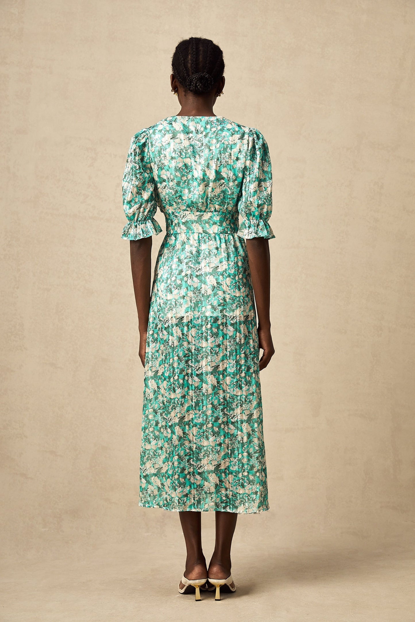 Woman wearing green floral print midi dress with high slit standing against plain background