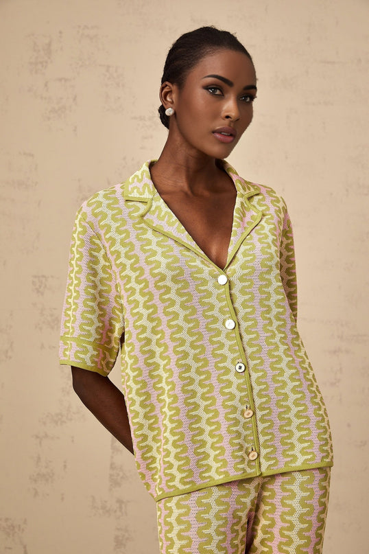 Woman wearing green knitted shirt and matching trousers color block design standing against plain background