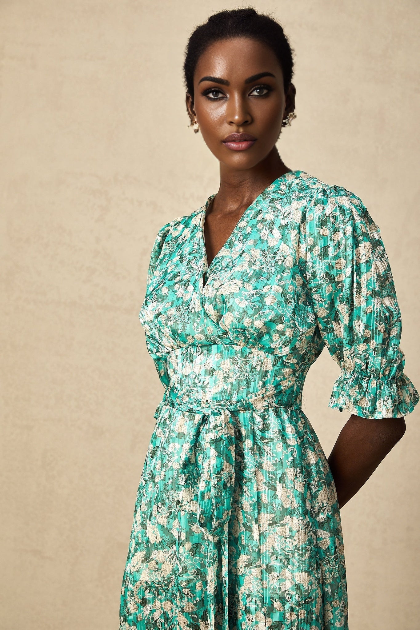 Woman wearing green midi dress with floral print and high slit standing against plain background