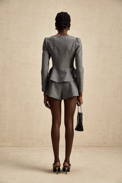 Woman wearing grey herringbone patterned top and matching shorts set standing against plain background