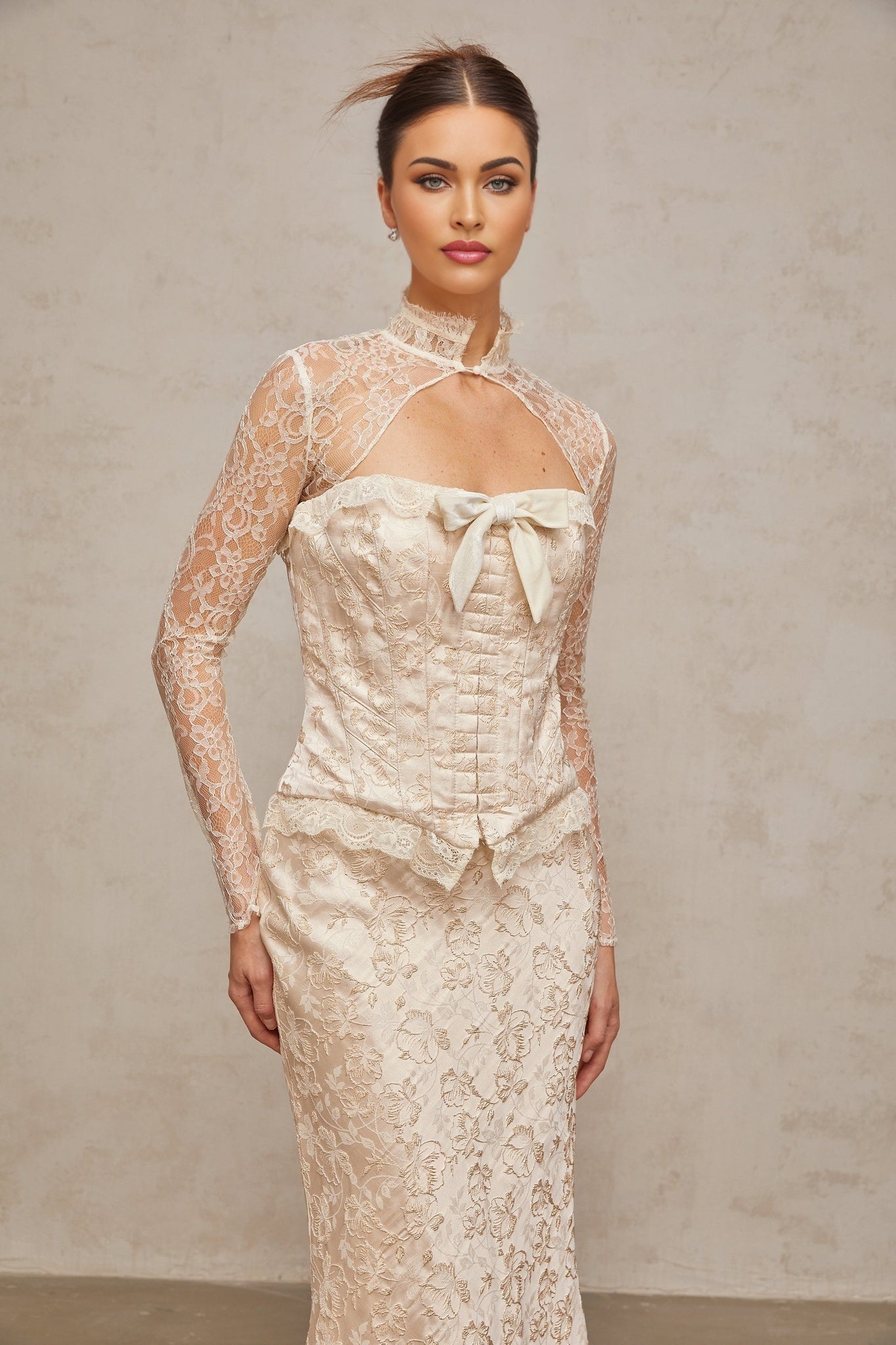 Woman wearing ivory colored matching set with patterned jacquard top and skirt standing against plain background