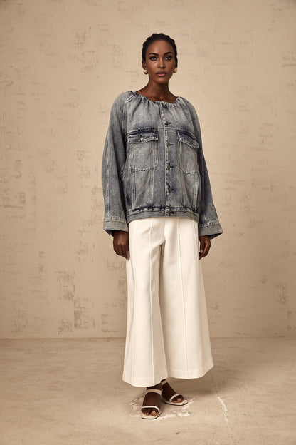 Woman wearing light blue collarless denim jacket with front pockets and button closure