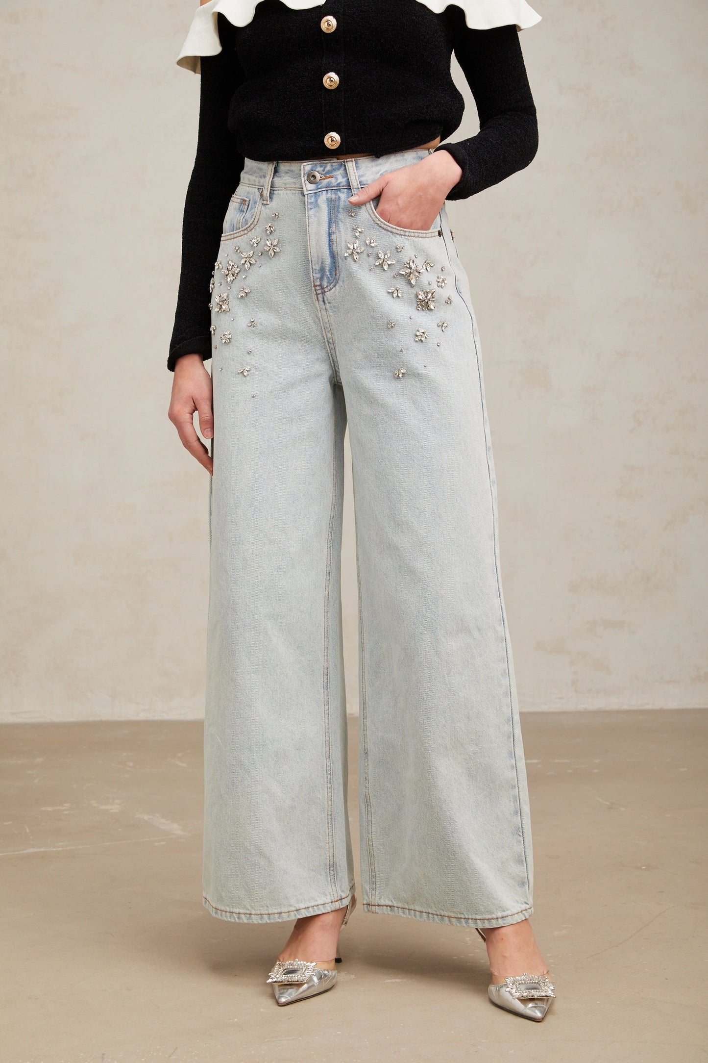 Woman wearing light blue jeans with decorative embellishments on the legs standing against a plain background