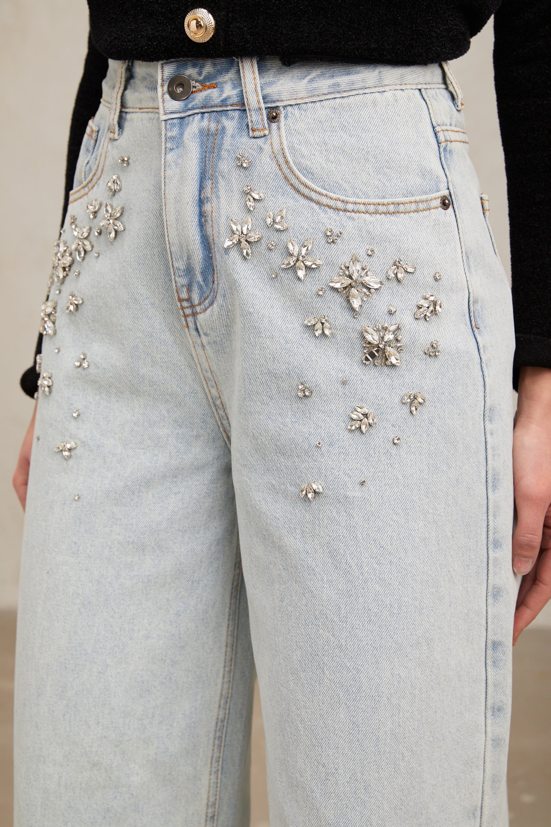 Woman wearing light blue jeans with decorative embellishments standing in relaxed pose