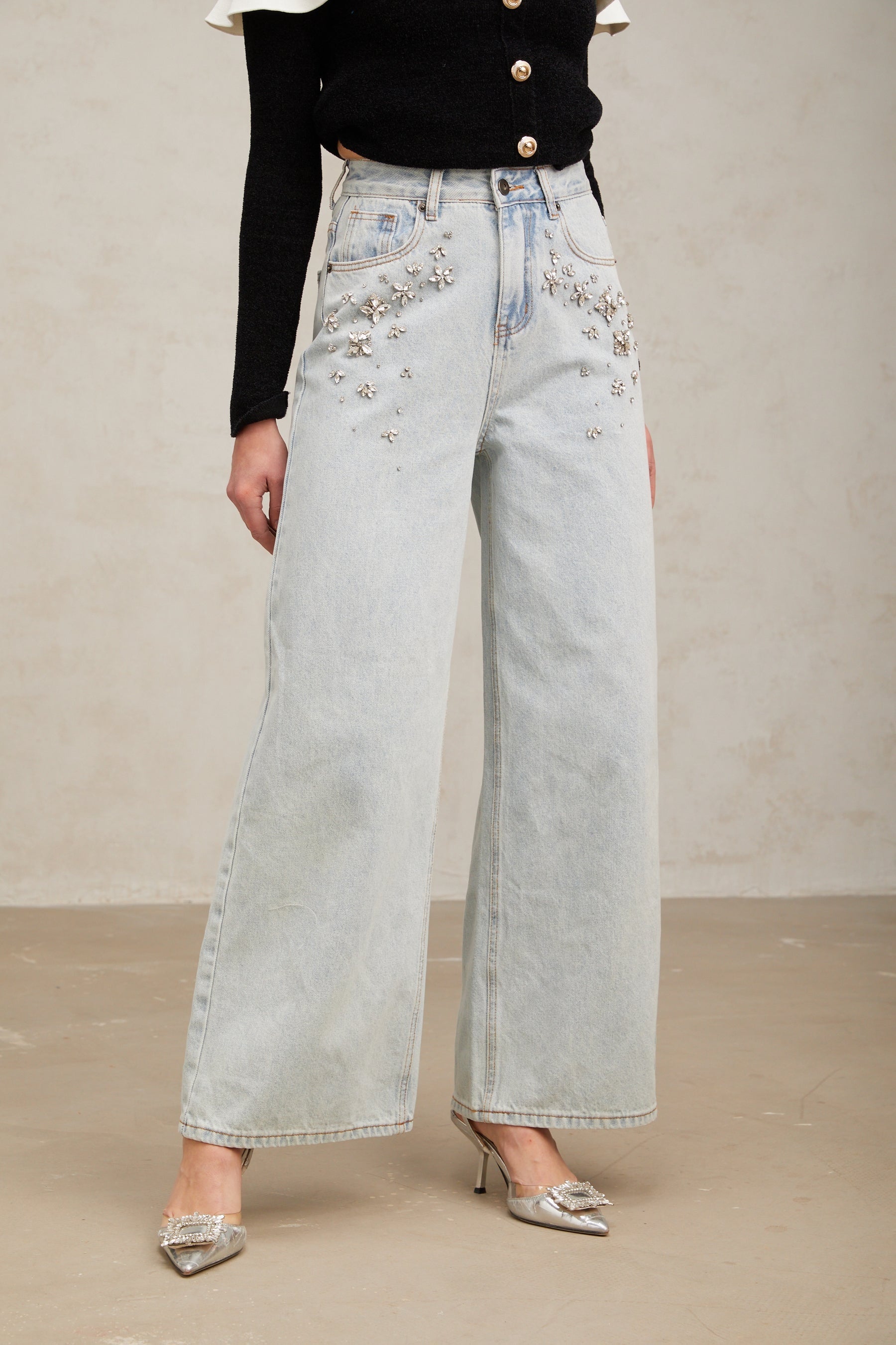 Woman wearing light blue jeans with embellishments standing against plain background