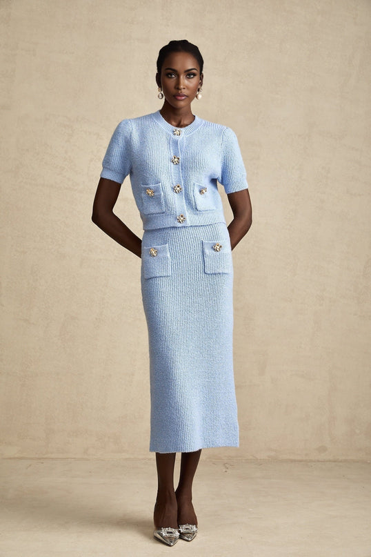 Woman wearing light blue knitted two piece outfit consisting of long sleeve blouse and midi skirt