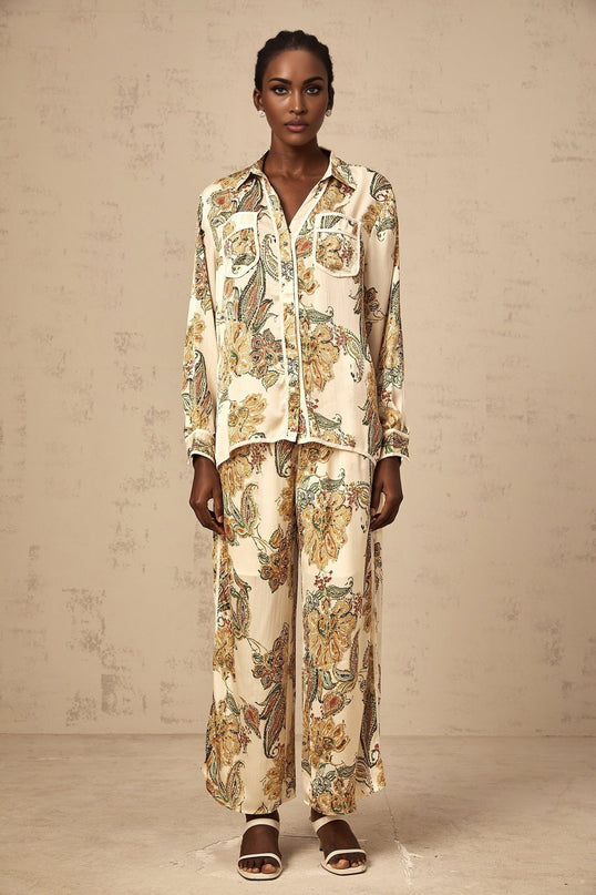 Woman wearing light colored floral print matching shirt and trousers set standing against neutral background